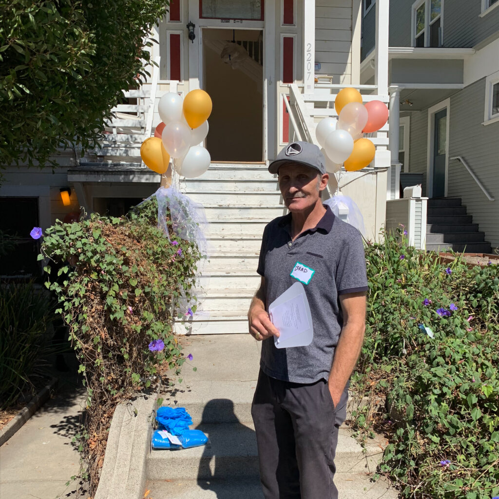 Almost Home Resident Manager stands on the sidewalk in front of the entrance of Almost Home. Balloons are attached to the railings on either side of the steps that lead to the front door.