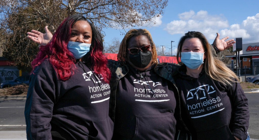 Three HAC staff wearing black sweatshirts that say, “Homeless Action Center”.