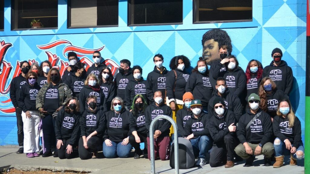 HAC staff posing in front of the West Oakland office. They are wearing masks and sweatshirts with HAC's logo.